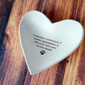 May include: White ceramic heart-shaped dish with the inscription "A faithful companion is always remembered in the love they leave in our hearts" and a paw print.