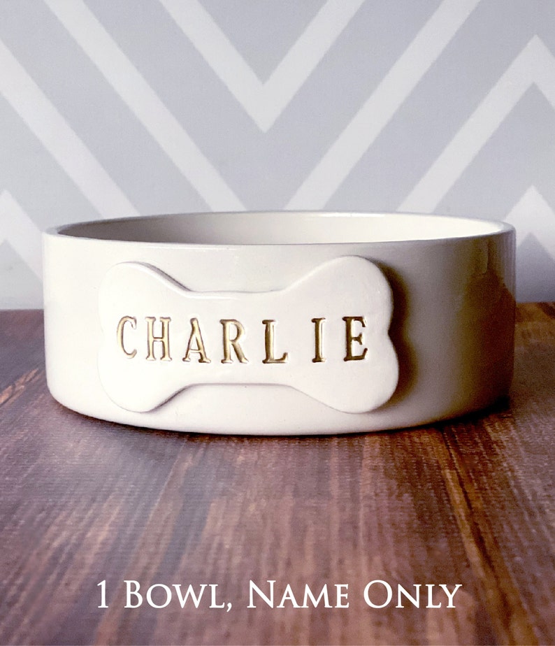 Image of the 1 bowl, name only option. One bowl is shown with a bone shaped tile on the front. The tile is stamped with the pet name in all capital letters and painted in metallic gold.