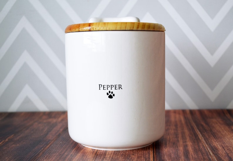 Puede incluir: Contenedor de comida para mascotas de cer&aacute;mica blanca con tapa de madera. El contenedor tiene la palabra "PEPPER" y una huella de pata en la parte delantera.