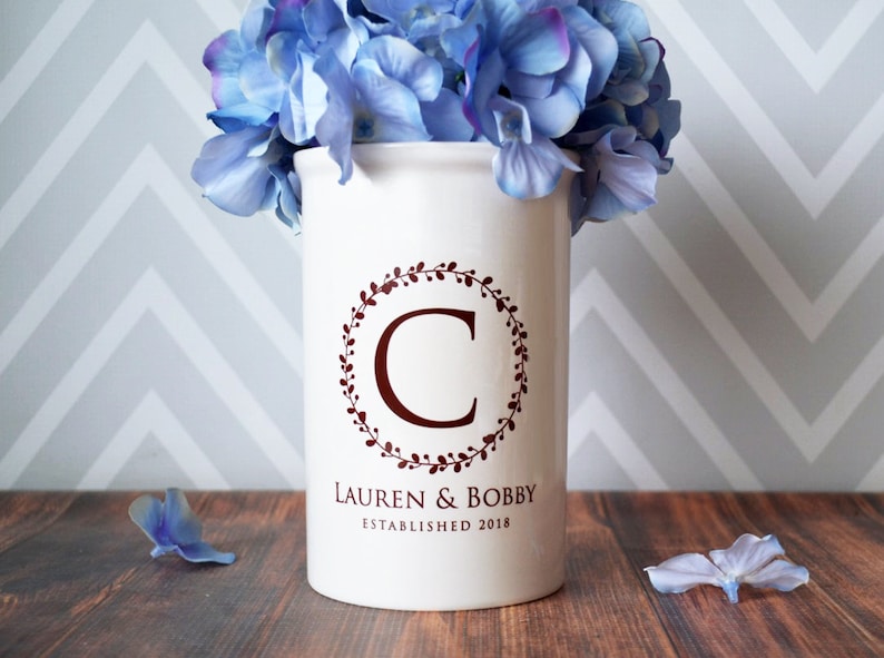 May include: White ceramic vase with a brown floral wreath and the letter C in the center. The vase also has the text "Lauren & Bobby Established 2018".