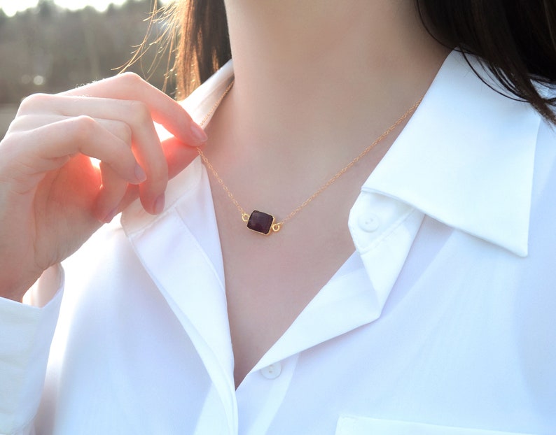 Puede incluir: Un collar de cadena dorada con un colgante rectangular negro.