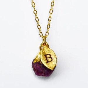Puede incluir: Collar de oro con un pequeño colgante de piedra preciosa púrpura facetada y un dije de hoja de oro con la letra "B" grabada.