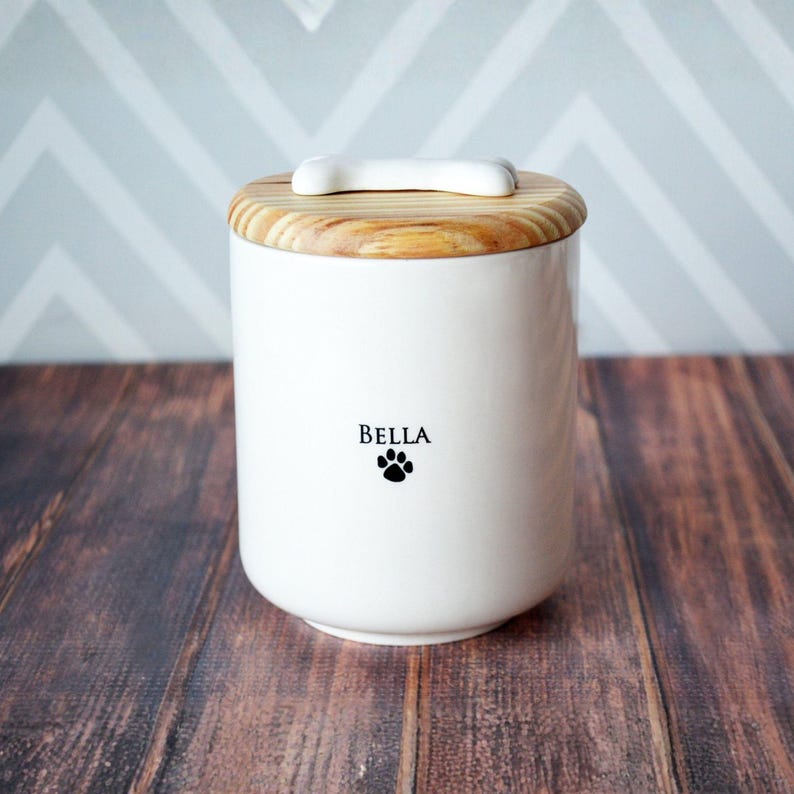 white ceramic pet urn for ashes with pet's name on front. dog bone tile on wood lid.
