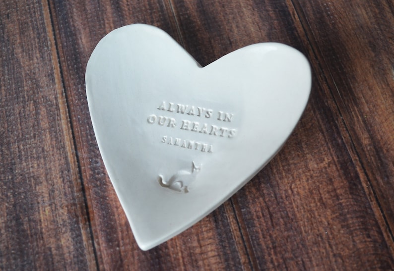 White ceramic heart-shaped dish with the inscription "Always in our hearts Samantha" and a small cat silhouette. Custom name.