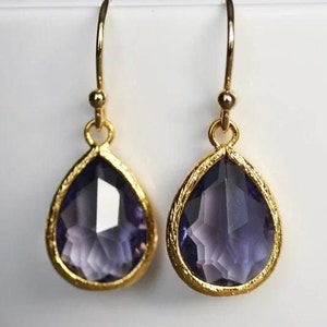 K&ouml;nnte beinhalten: Ein Paar goldene Tropfenohrringe mit violetten facettierten Glassteinen.
