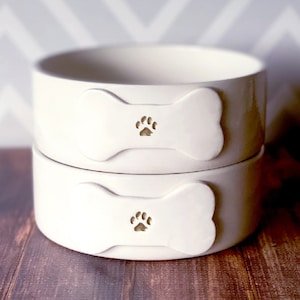 Image of the 2 bowls, paw only option. Two identical bowls are shown, each with a bone shaped tile on the front. Each bowl tile is stamped with a paw print image painted in metallic gold. The bowls are shown stacked on top of each other.