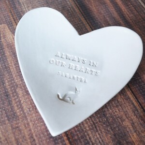 May include: White ceramic heart-shaped dish with the inscription "Always in our hearts" and the name "Samantha" below. A small cat silhouette is embossed in the center.