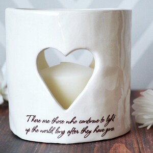 White ceramic candle holder with a heart-shaped cutout. The holder has the text "There are those who continue to light up the world long after they have gone." printed on the side.
