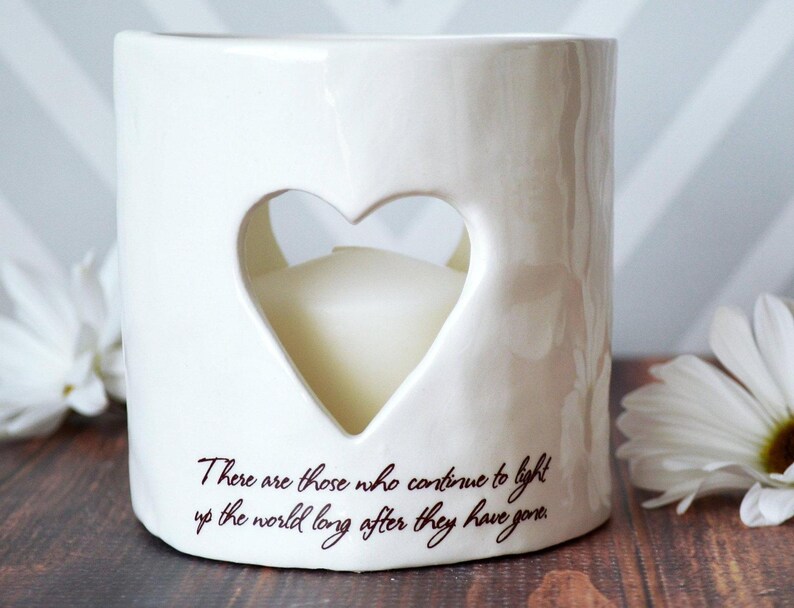 White ceramic candle holder with a heart-shaped cutout. The holder has the text "There are those who continue to light up the world long after they have gone." printed on the side.