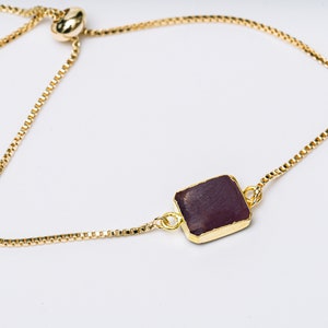 A gold chain bracelet with a square-shaped ruby gemstone pendant.