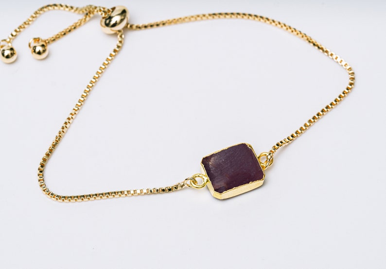 A gold chain bracelet with a square-shaped ruby gemstone pendant.