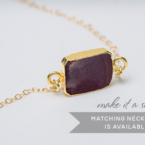 Puede incluir: Una pulsera de cadena dorada con un colgante rectangular de piedra preciosa p&uacute;rpura. El texto "make it a set! MATCHING NECKLACE IS AVAILABLE" est&aacute; debajo de la pulsera.
