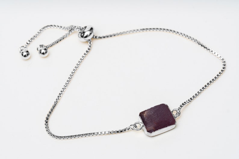 A silver chain bracelet with a dark red square gemstone pendant. The bracelet has a sliding clasp for adjustable sizing.