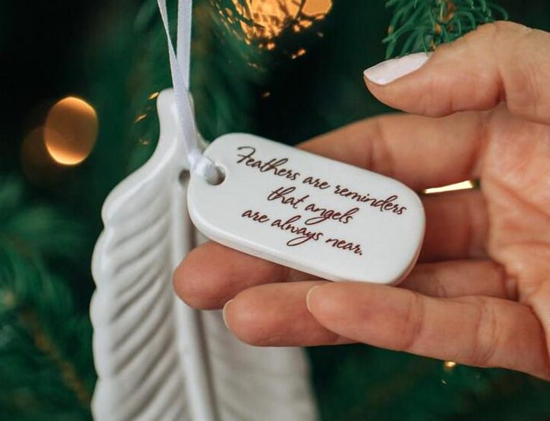 May include: White ceramic feather ornament with a white ribbon and a tag that reads "Feathers are reminders that angels are always near."