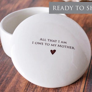 May include: White ceramic trinket box with a lid. The lid has the text "All that I am I owe to my mother." with a small heart.