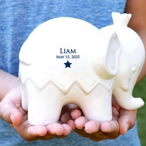 Peut inclure: Figurine d'&eacute;l&eacute;phant en c&eacute;ramique blanche avec un motif en zigzag sur le corps. Le texte "LIAM MAY 15, 2025" est imprim&eacute; en bleu marine. L'&eacute;l&eacute;phant est tenu dans les mains.