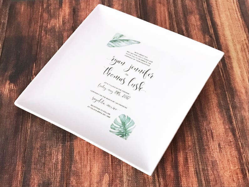 May include: White square ceramic plate with a wedding invitation printed on it. The invitation features a tropical leaf design and the text "With great joy we card you to celebrate the marriage of Ryan Thomas to Jennifer Lush at 4 o'clock in the evening Friday, May 19th, 2017 Ceremony on the beach of Las Palmas Sayulita, Mexico Reception to follow at Palapa Bonita del Mar"