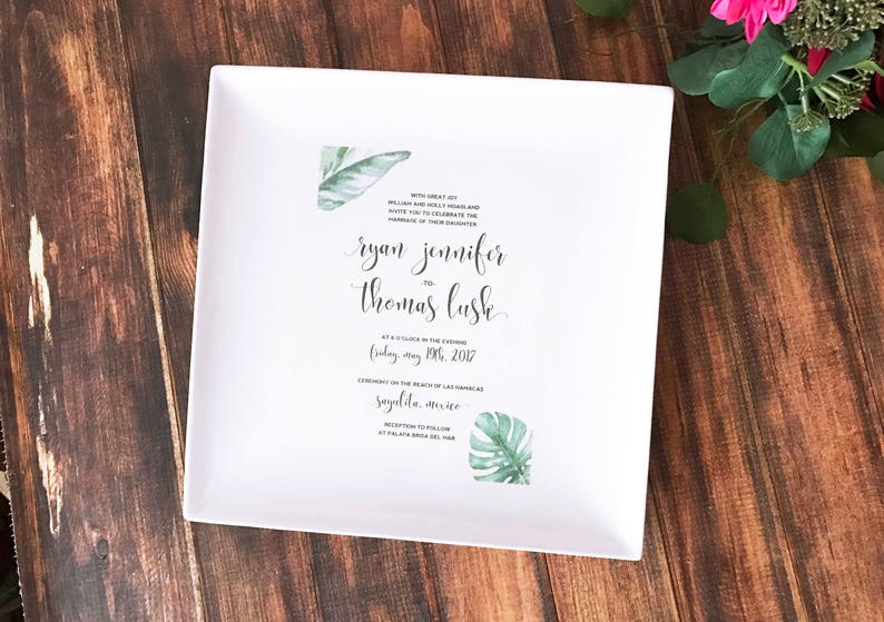 May include: White wedding invitation with green tropical leaf illustrations. The invitation reads "With great joy,  William and Holly Harris are delighted to celebrate the marriage of their daughter, Ryan Jennifer to Thomas Lusk, at 6 o'clock in the evening, Friday, May 19th, 2017, Ceremony on the beach of Las Marietas, Sayulita, Mexico, Reception to follow at Palapa Bonita del Mar."