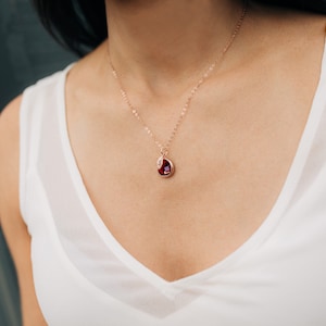 May include: A rose gold necklace with a teardrop-shaped pendant featuring a red gemstone.