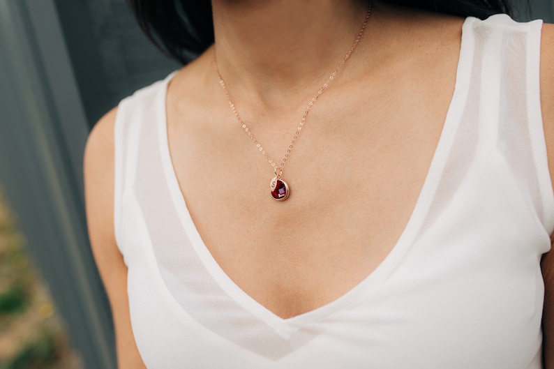 May include: A rose gold necklace with a teardrop-shaped pendant featuring a red gemstone.