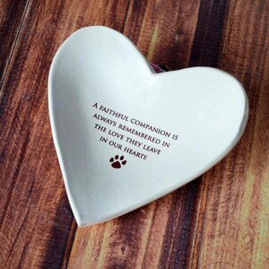 May include: White ceramic heart-shaped dish with the inscription "A faithful companion is always remembered in the love they leave in our hearts" and a paw print.