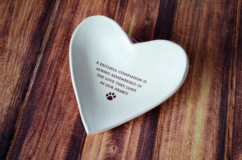 May include: White ceramic heart-shaped dish with the inscription "A faithful companion is always remembered in the love they leave in our hearts" and a paw print.