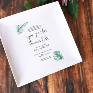 May include: White ceramic square plate with a wedding invitation printed on it. The invitation features a tropical theme with green leaves and the text "With great joy, William and Holly Fraser invite you to celebrate the marriage of their daughter, ryan jennifer to thomas lush, at 5 o'clock in the evening, Friday, May 19th, 2017, Ceremony on the beach of Las Hadas, Sayulita, Mexico, Reception to follow at Palapa Bar, Sayulita, Mex"