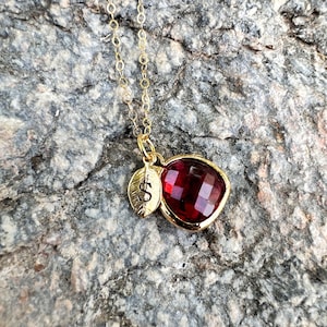 May include: A gold chain necklace with a red heart-shaped pendant and a small gold leaf charm with the letter 'S' engraved on it.