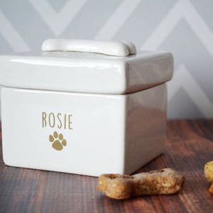 White ceramic pet food container with a bone-shaped lid. The container has the name "Rosie" and a paw print design in gold.