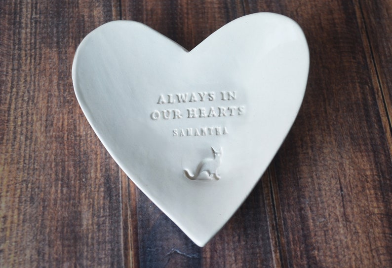 White ceramic heart-shaped dish with the text "Always in our hearts Samantha" and a small cat silhouette.