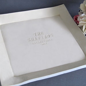 A handmade, white ceramic tray with a raised border. The tray has personalized text embossed on the surface.