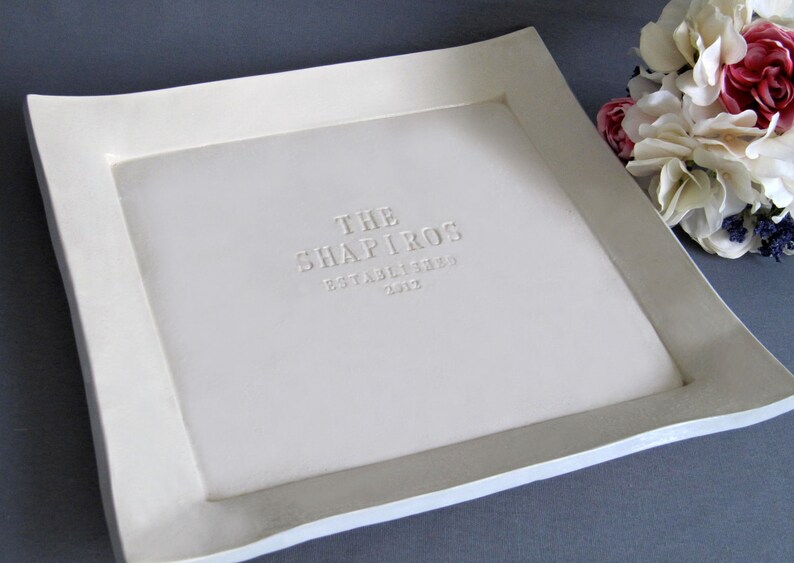 A handmade, white ceramic tray with a raised border. The tray has personalized text embossed on the surface.