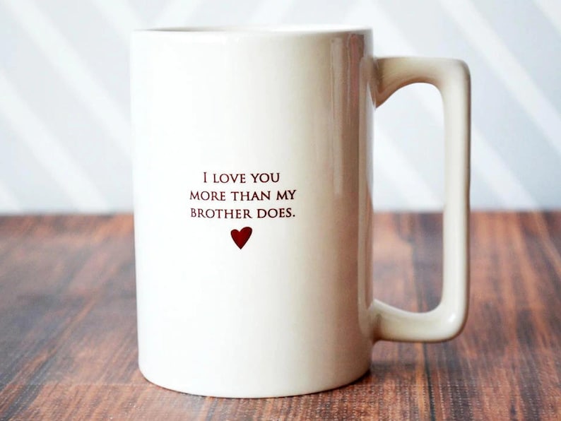 White ceramic mug with a heart and the text "I love you more than my brother does."