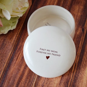 K&ouml;nnte beinhalten: Wei&szlig;e Keramik-Schmuckschatulle mit Deckel. Der Deckel tr&auml;gt den Text "First my mom, forever my friend" mit einem kleinen roten Herz.