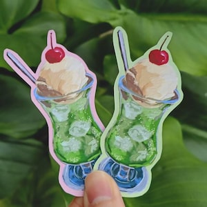 May include: Two die-cut stickers featuring a green soda float in a glass with a scoop of vanilla ice cream, a red cherry on top, and a silver straw. One sticker has a light pink border, and the other has a light green border, both showing ice cubes.