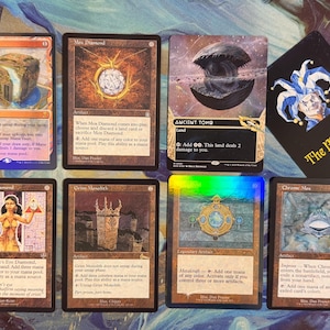 May include: A collection of seven Magic: The Gathering trading cards including Mana Vault, Mox Diamond, Ancient Tomb, Lion's Eye Diamond, Grim Monolith, Mox Opal, and Chrome Mox, alongside a black card featuring a jester and The Magic Lair text.
