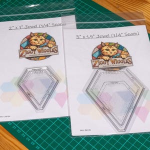 May include: Two clear acrylic quilting templates in plastic sleeves, labelled 2 inch by 1 inch and 3 inch by 1.5 inch jewel shapes with 1/4 inch seam allowances. Each features a Ziggy Wiggles logo with a cat illustration and SKU numbers.