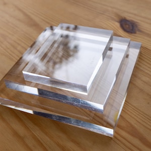 May include: A set of three stacked square clear acrylic blocks of varying sizes. Each block features a smooth, transparent surface with polished edges, arranged in a tiered formation from the largest base to the smallest top piece.