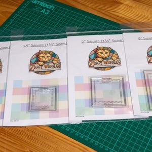 May include: Four clear acrylic square quilting templates labelled 1 inch, 1.5 inch, 2 inch, and 3 inch square with 1/4 inch seam allowance. Each template is packaged in a clear plastic sleeve with a Ziggy Wiggles logo featuring a cat illustration.