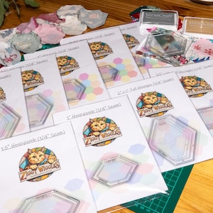 May include: A collection of clear acrylic quilting templates for hexagons and honeycombs, each packaged with a paper instruction sheet featuring the Ziggy Wiggles cat logo. Two VersaCraft ink pads and various fabric scraps are scattered nearby.