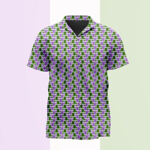 Puede incluir: Una camisa de manga corta con botones que presenta un patrón geométrico repetitivo de pequeños rectángulos verdes y morados sobre un fondo blanco. La camisa tiene un cuello clásico, una tapeta frontal con botones visibles y un dobladillo recto.
