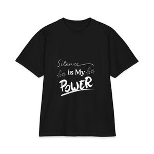 Könnte beinhalten: Ein schwarzes Kurzarm-T-Shirt mit weißem Text, der Silence is My POWER lautet, ergänzt durch kleine Stern-Grafiken. Das Design ist mittig auf der Brust platziert und verwendet eine Mischung aus Schreibschrift und fetten Pinselstrich-Buchstaben.