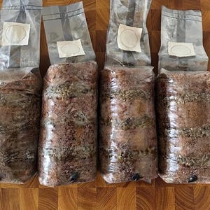 Può includere: Quattro sacchetti di plastica trasparente riempiti con un substrato marrone dalla consistenza granulosa. Ogni sacchetto è sigillato e presenta un filtro quadrato bianco vicino alla parte superiore. Il contenuto è materia organica con grani.