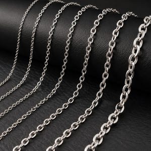 Pode incluir: Uma coleção de seis correntes de metal em tom prateado dispostas em fila, cada uma com um tamanho de elo distinto. As correntes variam de elos muito finos e delicados à esquerda para elos ovais mais grossos e substanciais à direita.