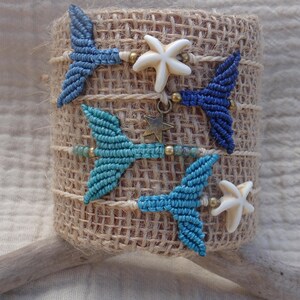 Può includere: Un set di tre braccialetti in macramè con cordino blu e turchese intrecciato a forma di coda di sirena. I braccialetti sono decorati con ciondoli a forma di stella marina bianca, piccole perline metalliche e una stella color bronzo.