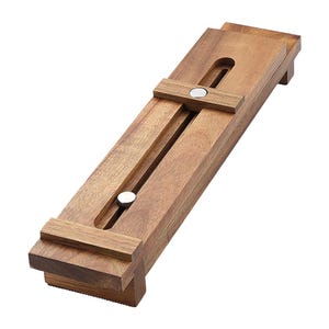 May include: A rectangular wooden adjustable stand featuring a natural brown grain finish. The stand includes a central slot with two sliding metal knobs that allow for width adjustment, supported by small feet at each end of the base structure.