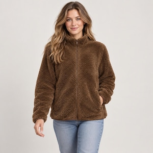 May include: A brown, long-sleeved, zip-up jacket made of a fuzzy, textured fleece material. The jacket features a high collar, a full-length front zipper, and two side pockets. It is worn over light blue denim jeans, creating a casual look.