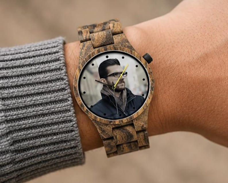 May include: A wristwatch with a brown wood grain finish on the case and link band. The watch face features a custom photographic print of a person wearing glasses and a dark jacket, with black hour markers and a bright yellow second hand.