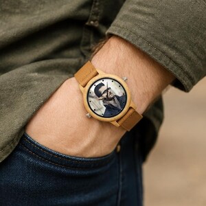 Pu&ograve; includere: Un orologio da polso con cassa in legno marrone chiaro e cinturino in pelle beige abbinato. Il quadrante dell'orologio presenta un ritratto fotografico personalizzato in bianco e nero di una persona con occhiali e lancette nere.