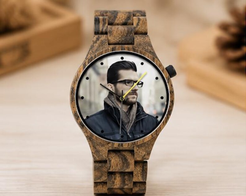 May include: A wristwatch with a dark brown wood grain case and matching link band. The watch face features a photographic portrait of a person wearing glasses and a dark jacket. It has black hour and minute hands and a bright yellow second hand.